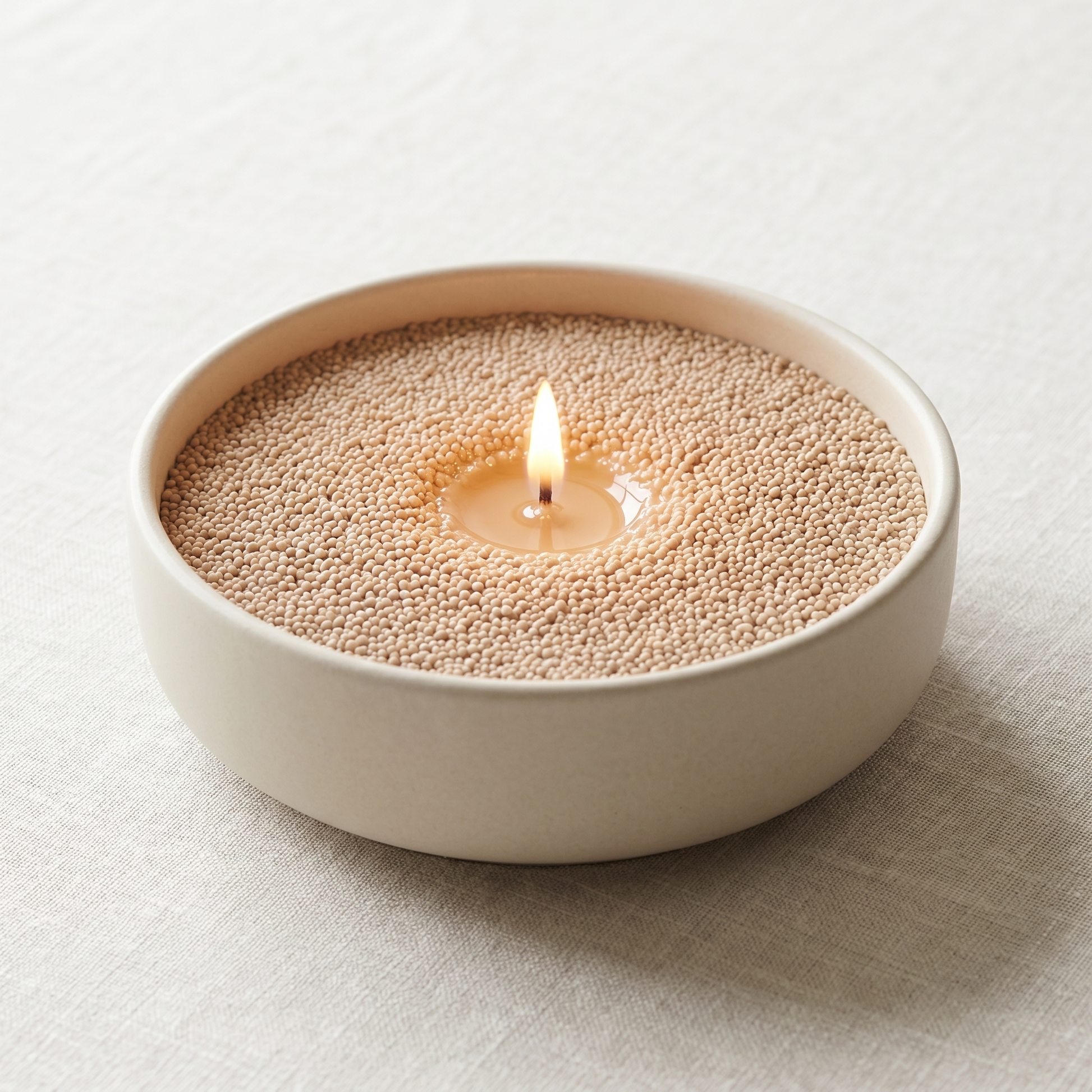 Coco Loco beige sand wax candle, lit, in a cream ceramic bowl