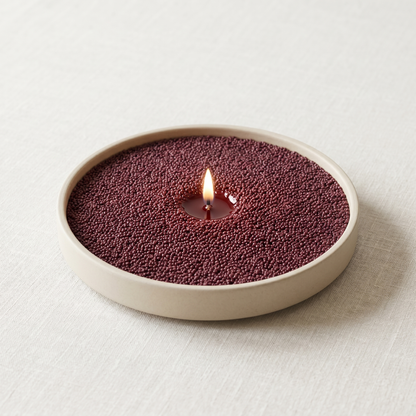 Drunken Pash wine-red passionfruit sand wax candle, lit, in a shallow round dish