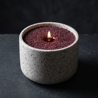 Drunken Pash wine-red sand wax candle, lit, in a terrazzo vessel on dark slate